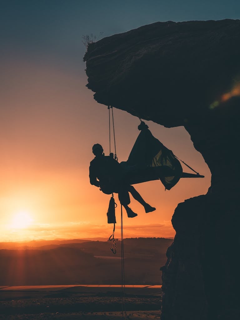 Person climbing a mountain at sunrise, symbolizing proactive achievement and determination.