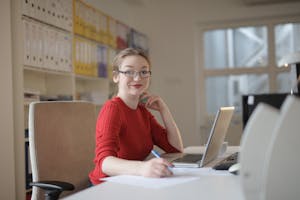 A person enthusiastically working at a desk with a laptop and notepad