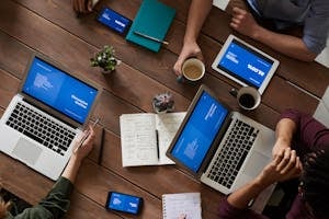 A professional office setting with a collaborative team working around a table with laptops and productivity tools visible.