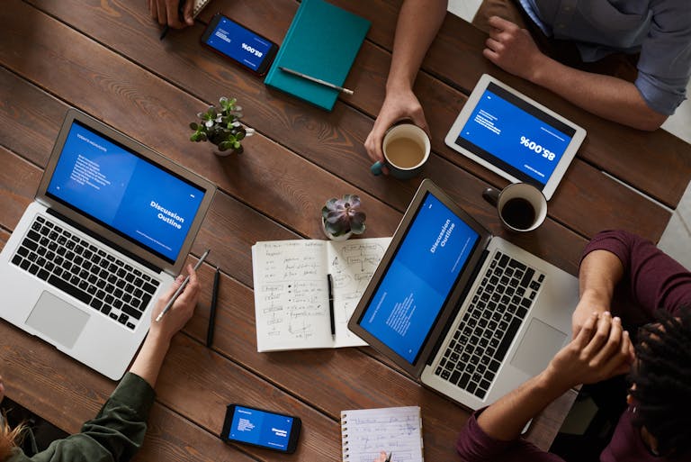A professional office setting with a collaborative team working around a table with laptops and productivity tools visible.