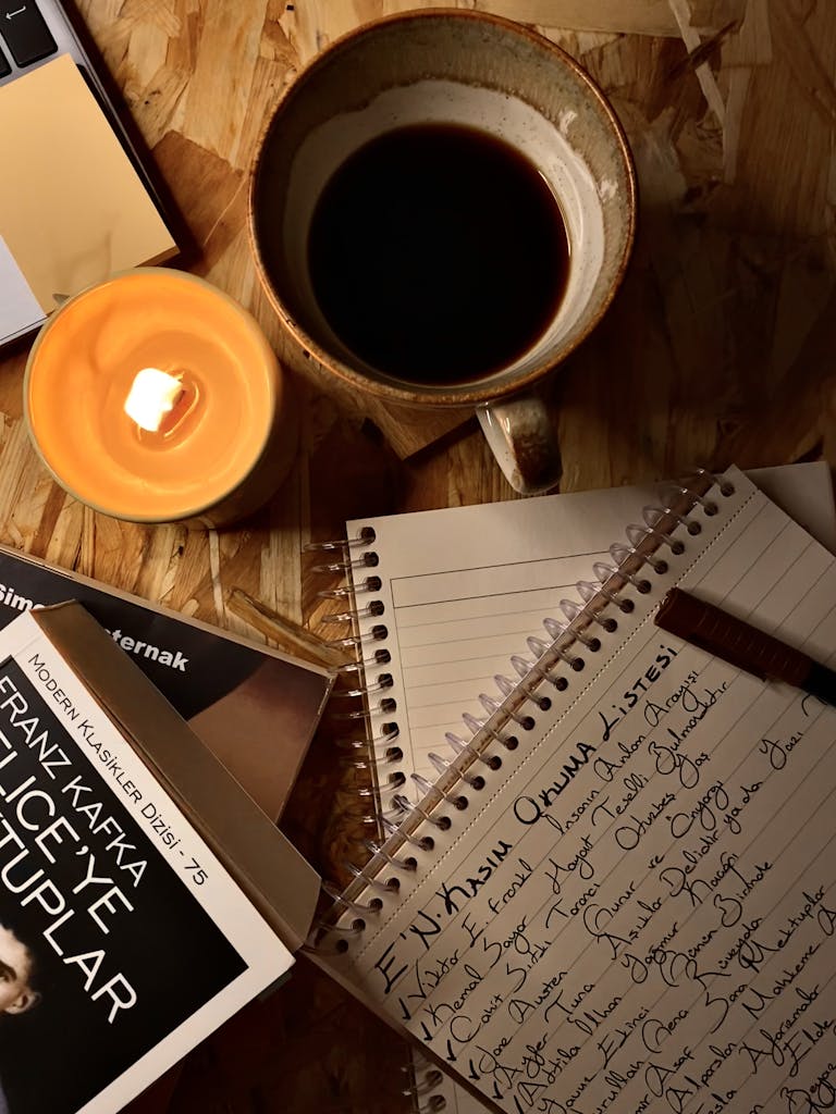 A hand writing in a journal beside a candle and coffee mug.