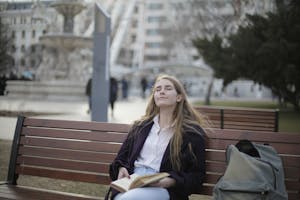 A serene individual sitting peacefully on a park bench, surrounded by nature, holding a cup of tea while traffic blurs in the background.