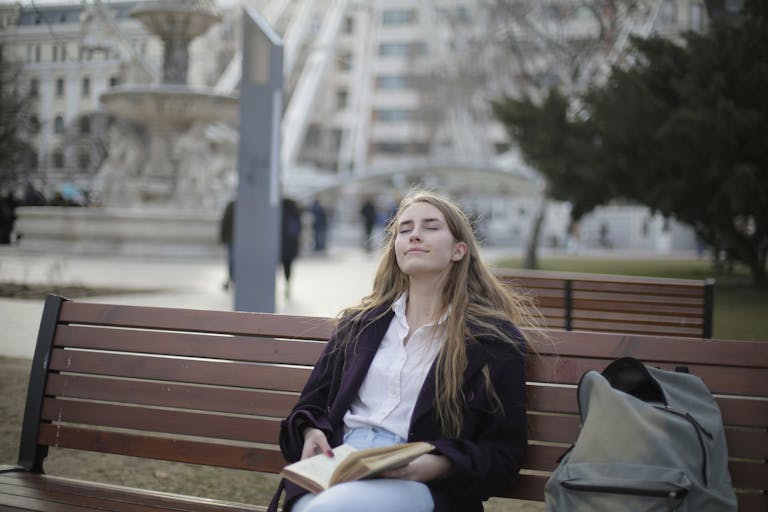 A serene individual sitting peacefully on a park bench, surrounded by nature, holding a cup of tea while traffic blurs in the background.