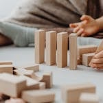 A hand placing a small domino that leads to progressively larger dominos — symbolizing micro actions leading to big results.