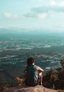 A person smiling, standing on top of a mountain or overlooking a city skyline, symbolizing optimism and achievement.
