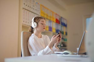 A person wearing noise-canceling headphones at a tidy desk with phone turned face down.
