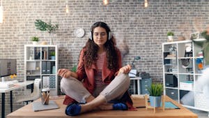 A person meditating at a desk while phones and notifications float around